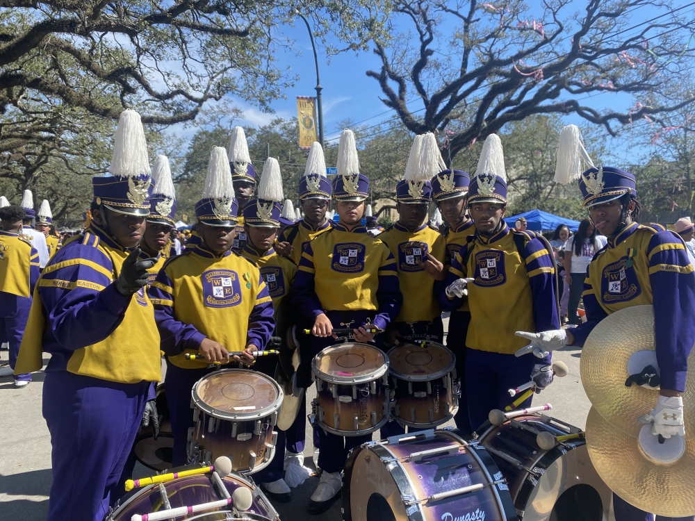 A group of young drummers in purple and gold band uniforms faces the camera. 